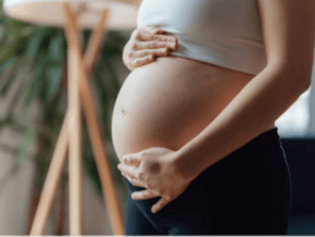 Mujer embarazada sosteniendo su vientre con ambas manos, vestida con camiseta blanca.