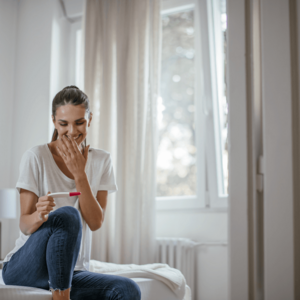 Mujer sentada en la cama sonriendo y mirando un test de embarazo