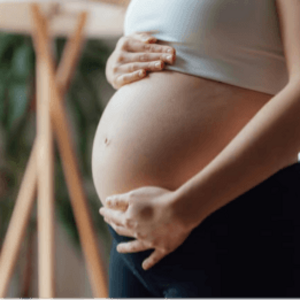Mujer embarazada sosteniendo su vientre con ambas manos, vestida con camiseta blanca.