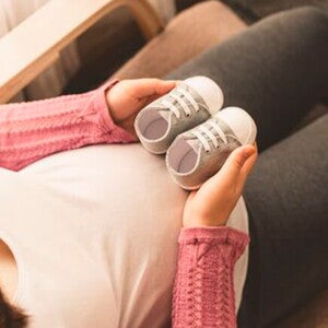 Mamá embarazada de un niño arcoíris cogiendo unos zapatitos.