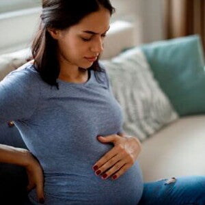 Mamá tocando el vientre y la espalda sintiendo molestia.