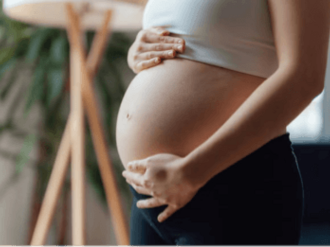 Mujer embarazada sosteniendo su vientre con ambas manos, vestida con camiseta blanca.