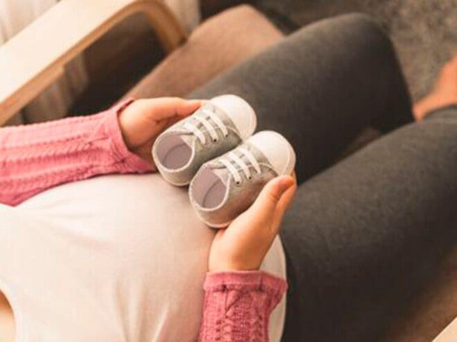 Mamá embarazada de un niño arcoíris cogiendo unos zapatitos.