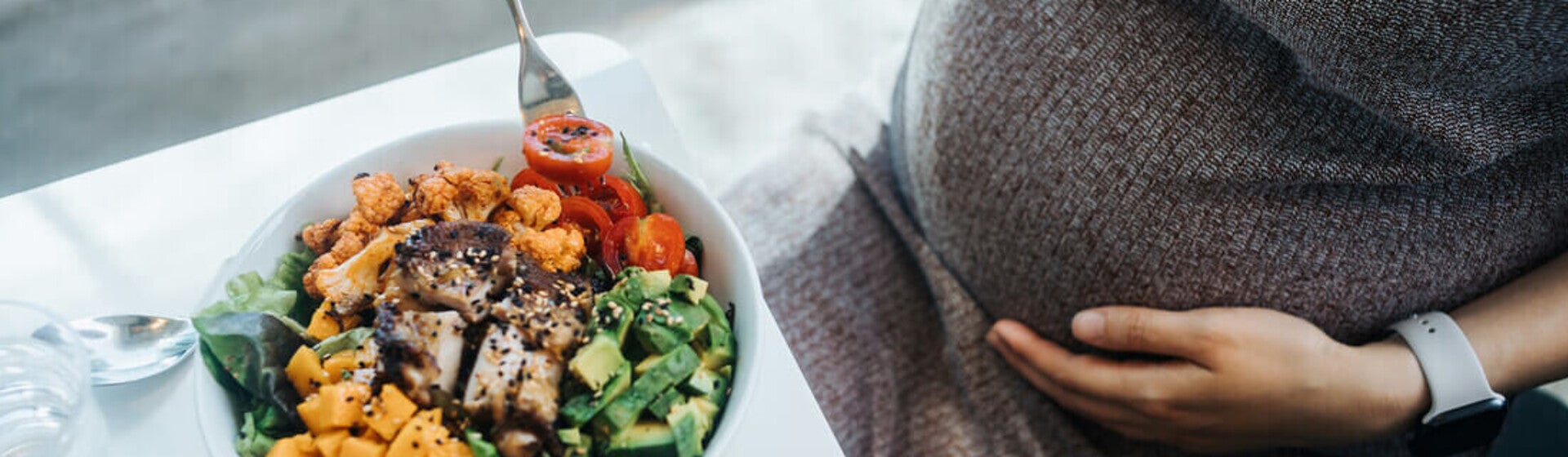 Mujer embarazada en la cocina comiendo ensalada con verduras variadas. Nutrición en el embarazo.