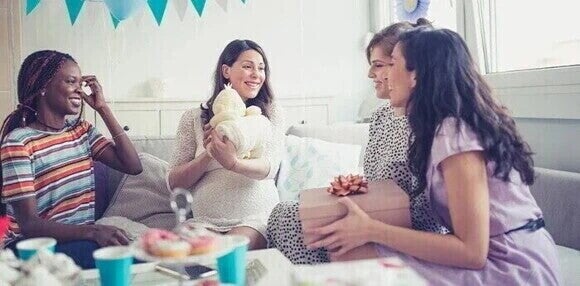 Futura mamá rodeada de amigas y abriendo regalos en fiesta de revelación de género del bebé